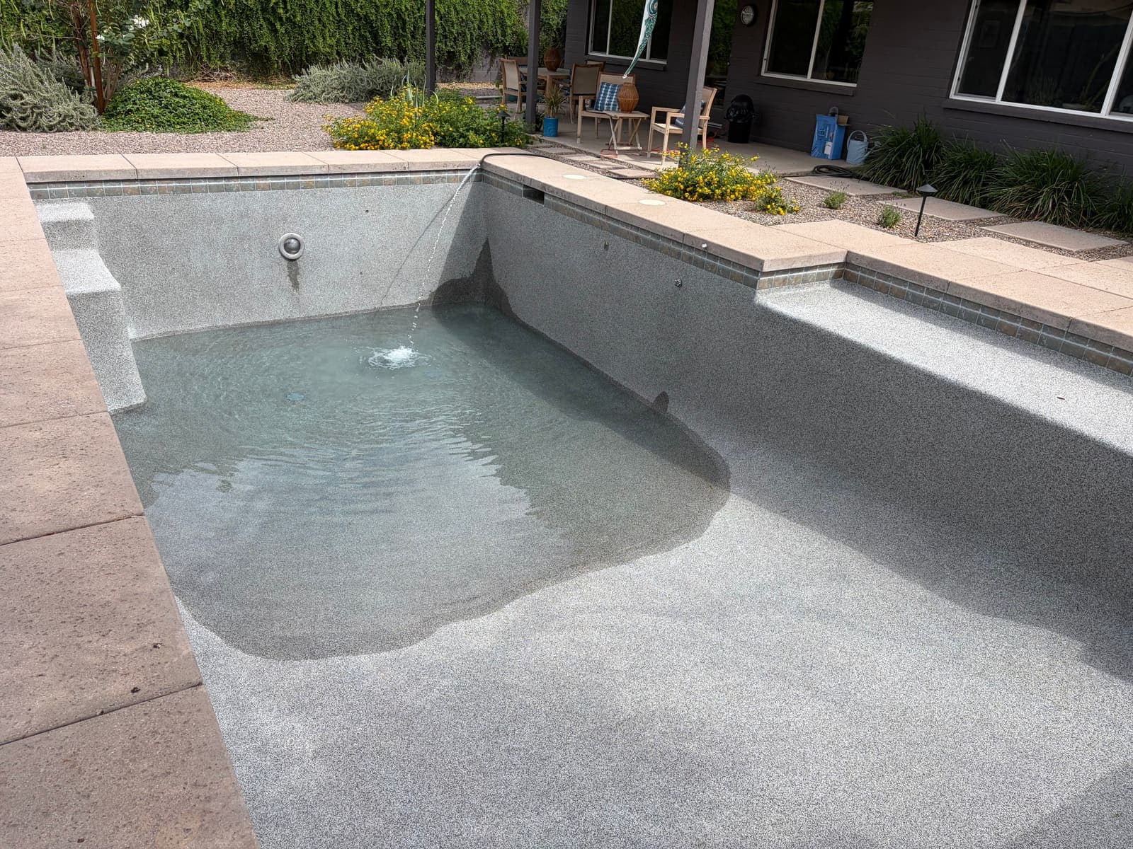 Clean gray pebble pool shell refilling after its chlorine wash, fill water rippling in the shallow end